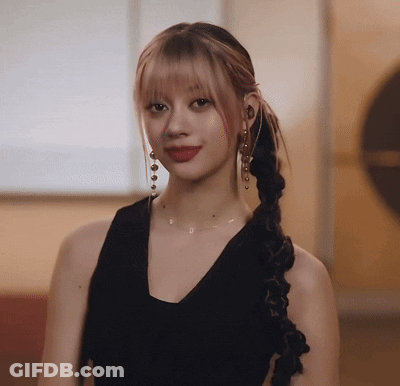 A Woman Wearing A Braided Ponytail And Earrings Is Looking At The Camera GIF