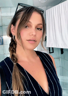 A Woman Wearing A Braided Ponytail And Hoop Earrings Takes A Selfie In A Bathroom GIF