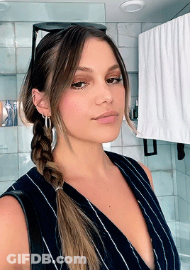 A Woman Wearing A Braided Ponytail Is Taking A Selfie In A Bathroom GIF