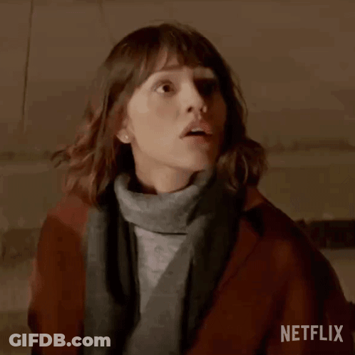 Woman In Brown Coat And Gray Sweater Standing In Dark Room GIF