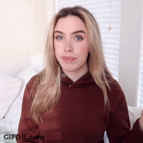 A Woman Wearing A Brown Hoodie Is Making A Silly Face GIF