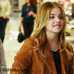 A Woman Wearing A Brown Jacket Is Smiling In A Store GIF