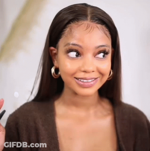 A Woman Wearing A Brown Sweater And Hoop Earrings Is Smiling And Looking To The Side . GIF