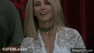 A Woman Wearing A Choker And A White Shirt Is Smiling While Sitting In A Theatre . GIF
