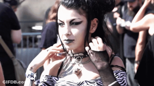 A Woman Wearing A Choker And A Zebra Print Top Is Standing In A Crowd GIF