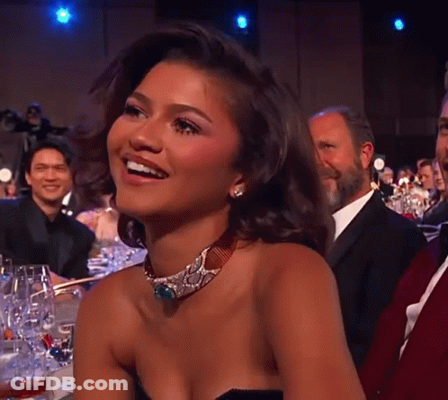 A Woman Wearing A Choker Is Smiling In Front Of A Crowd Of People GIF