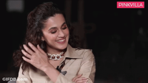 A Woman Wearing A Choker Is Smiling In Front Of A Pinkvilla Ad GIF
