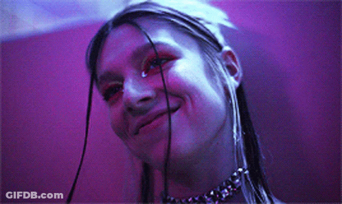 A Woman Wearing A Choker Is Smiling In Front Of A Purple Wall GIF