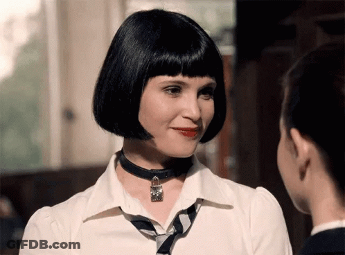 A Woman Wearing A Choker Necklace And A White Shirt Looks At Another Woman GIF