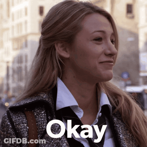 A Woman Wearing A Coat And Tie Is Smiling With The Word Okay Below Her GIF