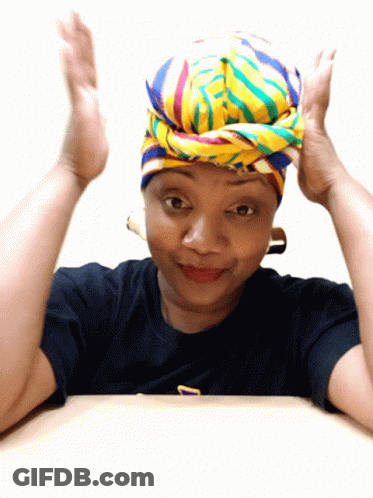 A Woman Wearing A Colorful Head Scarf And A Black Shirt With The Letter T On It GIF