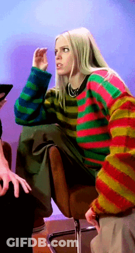 A Woman Wearing A Colorful Striped Sweater Is Sitting In A Chair GIF