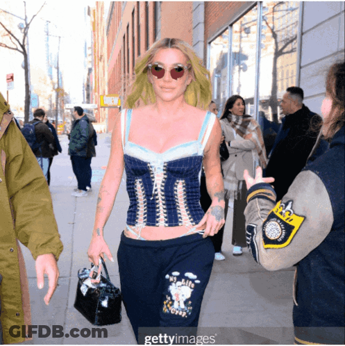 A Woman Wearing A Corset Top And Sweatpants Walking Down A Street GIF