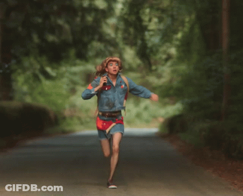 A Woman Wearing A Cowboy Hat And A Denim Jacket Runs Down A Road GIF