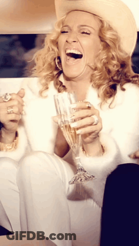 A Woman Wearing A Cowboy Hat Is Holding A Glass Of Champagne GIF