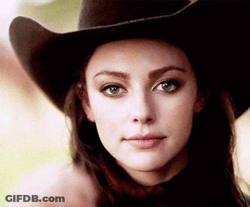 A Woman Wearing A Cowboy Hat Is Looking At The Camera . GIF