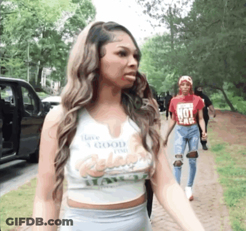 A Woman Wearing A Crop Top That Says Have A Good Time Is Walking Down A Sidewalk . GIF