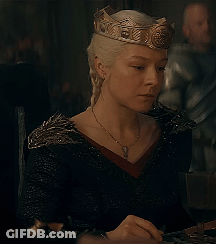 A Woman Wearing A Crown And A Black Dress Is Sitting At A Table GIF