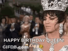 A Woman Wearing A Crown And A Necklace Is Standing In Front Of A Crowd Of People . GIF