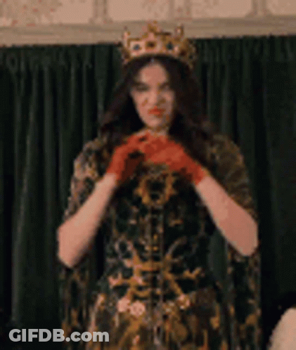 A Woman Wearing A Crown And Red Gloves Is Standing In Front Of A Curtain . GIF