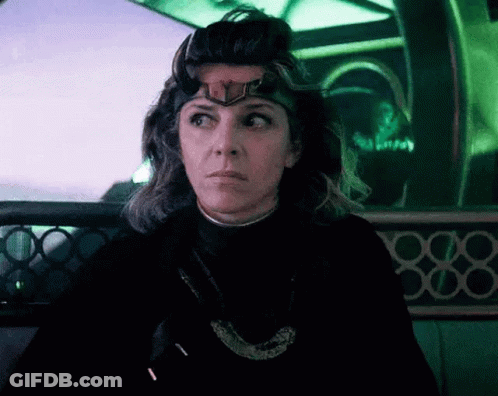 A Woman Wearing A Crown On Her Head Is Sitting In A Dark Room . GIF