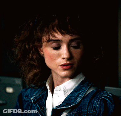 A Woman Wearing A Denim Jacket And White Shirt Looks Down GIF