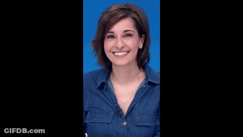 A Woman Wearing A Denim Shirt And A Necklace Is Smiling Against A Blue Background . GIF