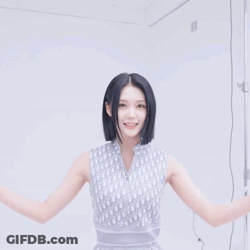 A Woman Wearing A Dior Sleeveless Top Smiles With Her Hands In The Air GIF