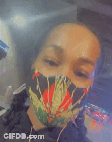 A Woman Wearing A Face Mask With A Spider On It Is Smoking A Cigarette . GIF