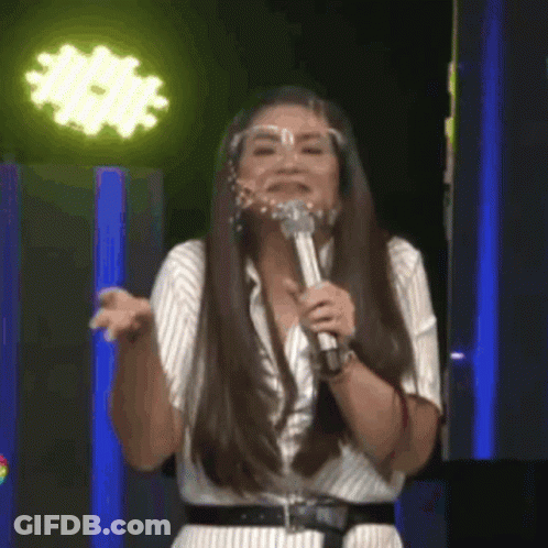 A Woman Wearing A Face Shield Is Singing Into A Microphone On A Stage . GIF
