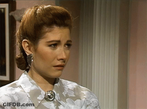 A Woman Wearing A Floral Shirt And Earrings Is Looking At The Camera GIF