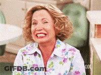 A Woman Wearing A Floral Shirt Is Laughing With Her Eyes Closed . GIF
