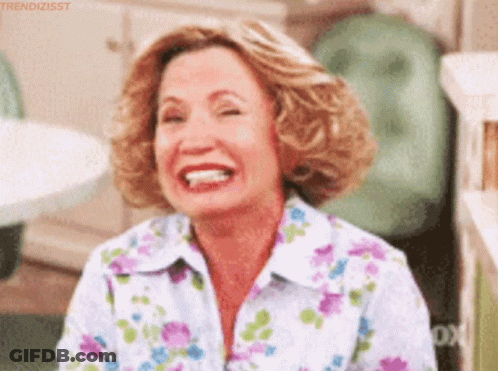 A Woman Wearing A Floral Shirt Is Laughing With Her Eyes Closed . GIF
