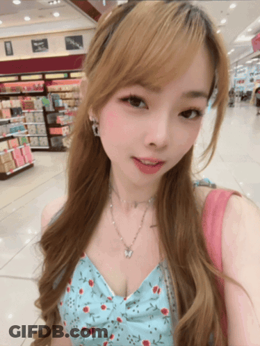 A Woman Wearing A Floral Top And A Butterfly Necklace Takes A Selfie GIF