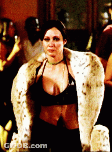 A Woman Wearing A Fur Coat And A Choker Stands In A Dark Room GIF