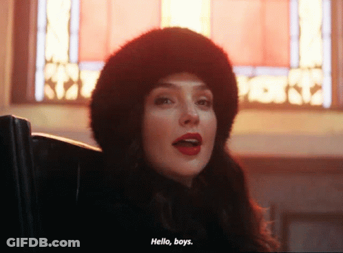 A Woman Wearing A Fur Hat Says Hello Boys In Front Of A Stained Glass Window GIF