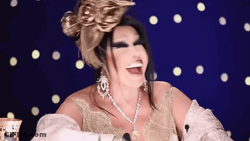 A Woman Wearing A Gold Dress And A Necklace Is Smiling And Laughing . GIF