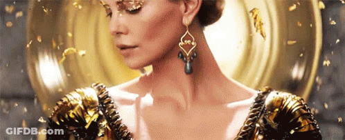 A Woman Wearing A Gold Dress And Earrings Is Standing In Front Of A Mirror . GIF
