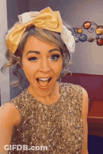A Woman Wearing A Gold Sequined Dress And A Yellow Bow In Her Hair GIF