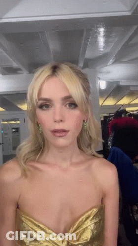 A Woman Wearing A Gold Strapless Dress Is Looking At The Camera GIF