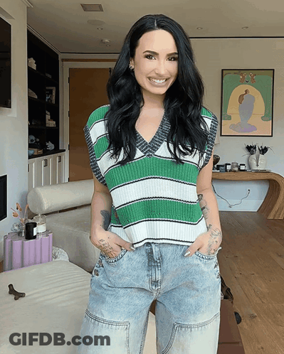 A Woman Wearing A Green And White Striped Vest And Jeans Smiles For The Camera GIF