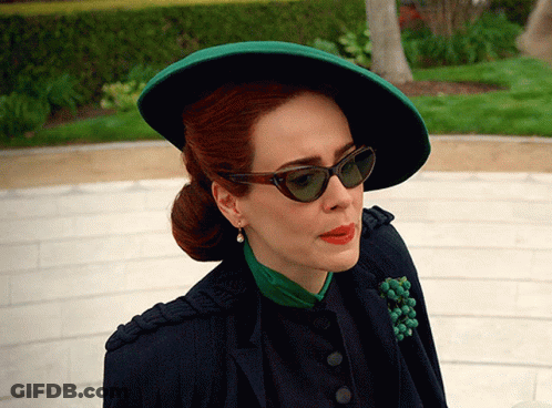 A Woman Wearing A Green Hat And Sunglasses Looks To Her Left GIF