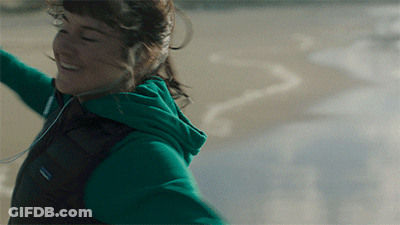 A Woman Wearing A Green Patagonia Vest Is Smiling On The Beach GIF