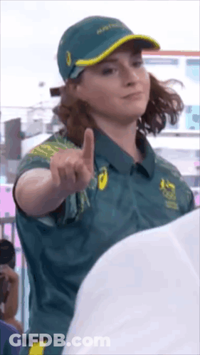 A Woman Wearing A Green Shirt And A Hat Is Pointing At The Camera GIF