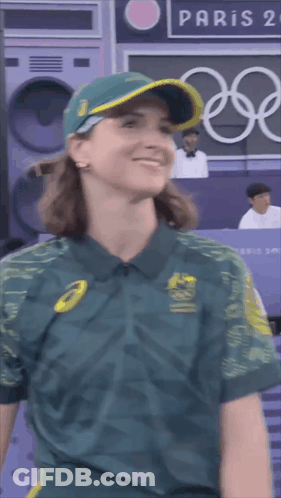 A Woman Wearing A Green Shirt And A Hat Is Smiling In Front Of A Paris Sign GIF