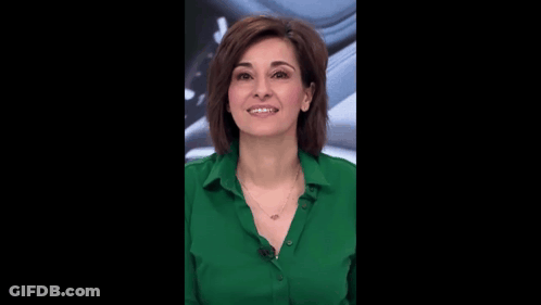 A Woman Wearing A Green Shirt And A Necklace Smiles GIF