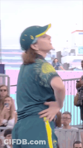 A Woman Wearing A Green Shirt And A Yellow Hat Is Standing With Her Hands On Her Hips GIF