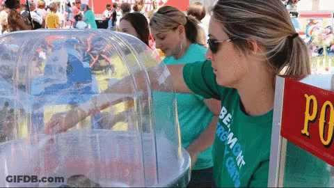 A Woman Wearing A Green Shirt That Says Burlington On It Stands In Front Of A Cotton Candy Machine GIF