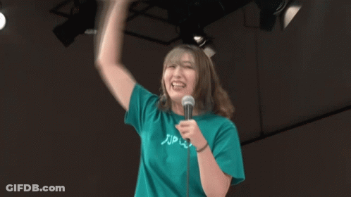 A Woman Wearing A Green Shirt That Says Zip On It Is Holding A Microphone GIF