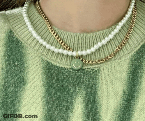 A Woman Wearing A Green Sweater And A Necklace With A Smiley Face On It . GIF